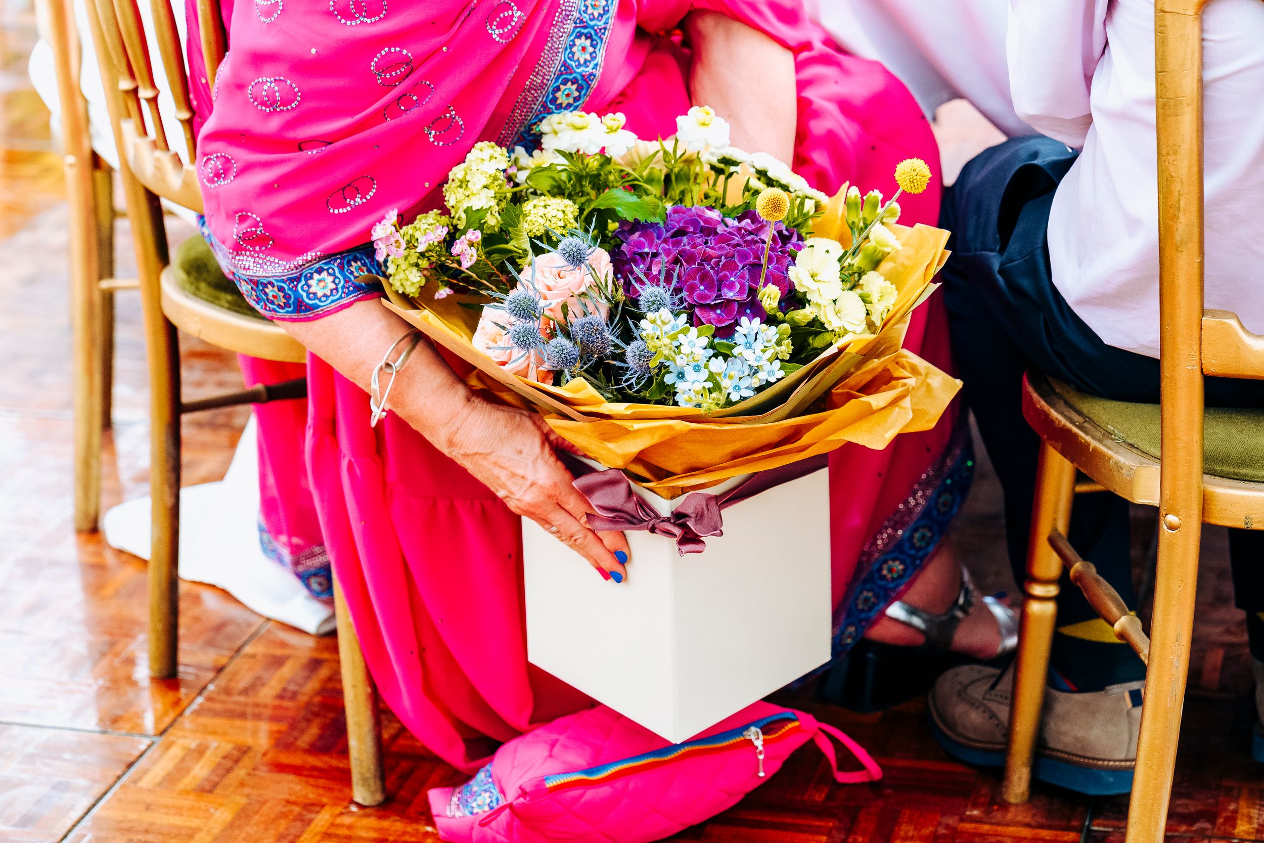 A wedding guest in a pink sari holds a beautiful bouquet of purple and yellow flowers.