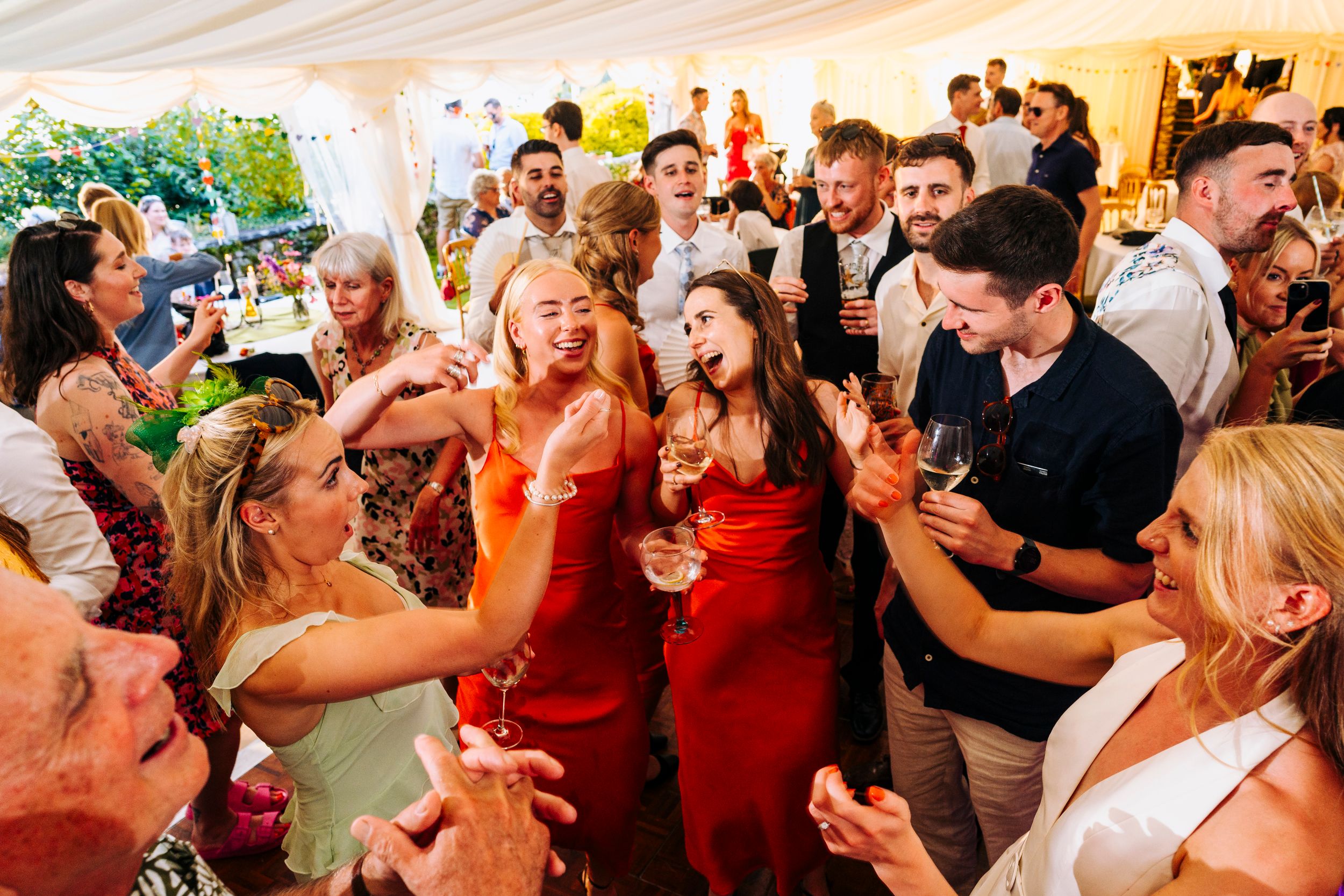 Joyful wedding guests dancing and celebrating together inside colorful marquee reception venue.