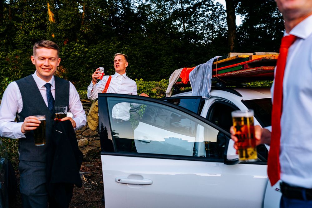 Smartly dressed wedding guests smiling and socializing beside white car at outdoor venue.