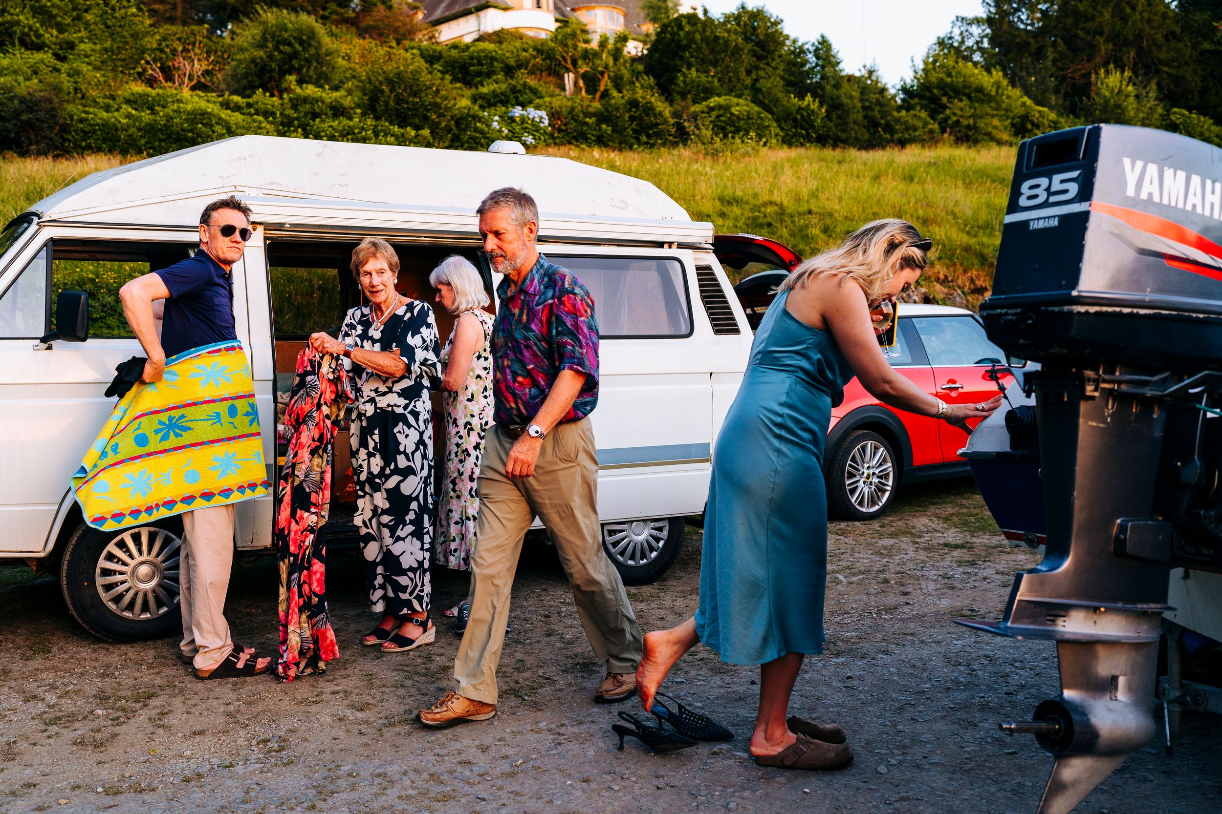 Group of friends unloading a white vintage van near a Yamaha boat engine at sunset.