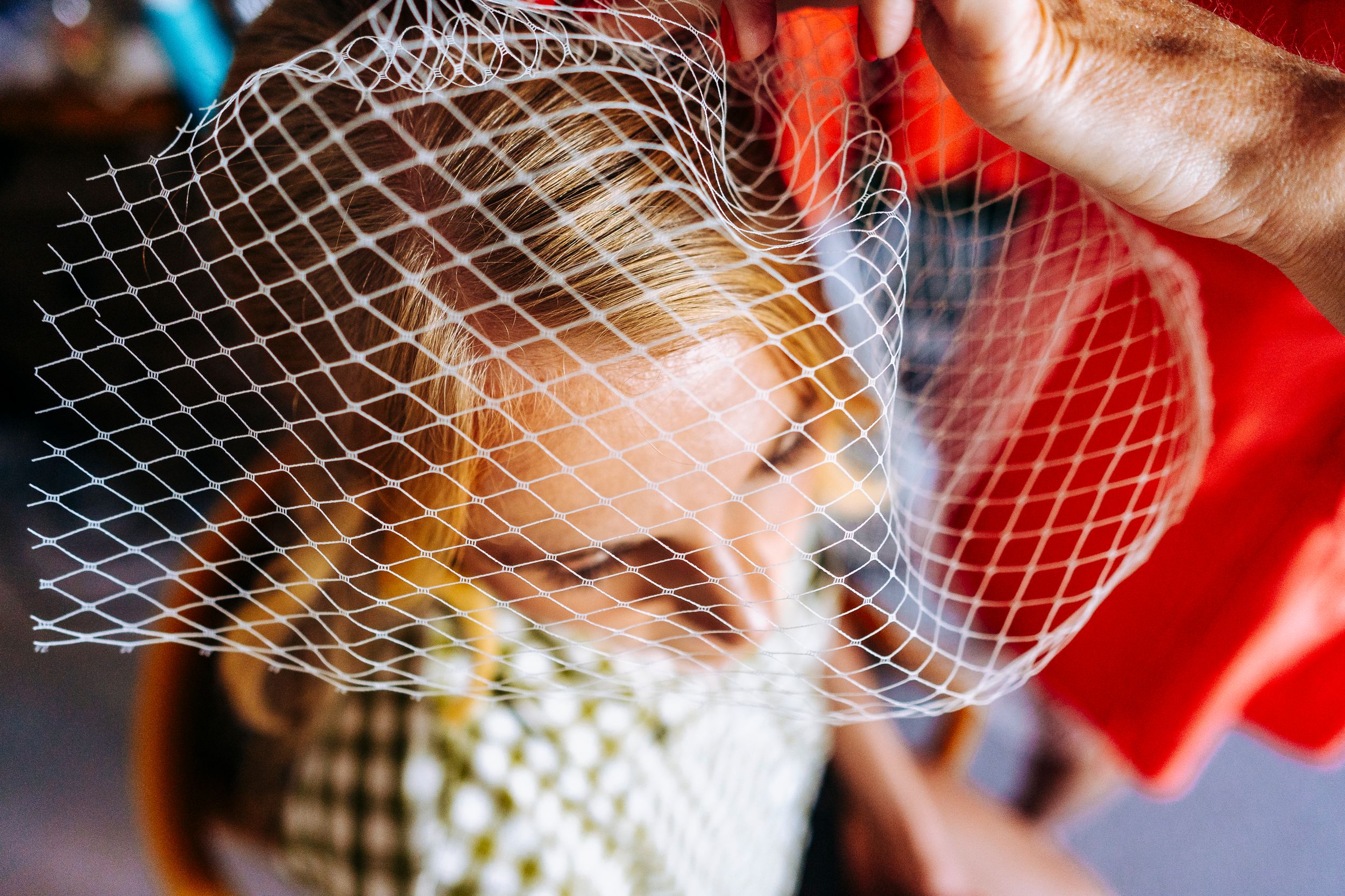 Close-up of a white birdcage veil being placed on a blonde brides head before wedding.