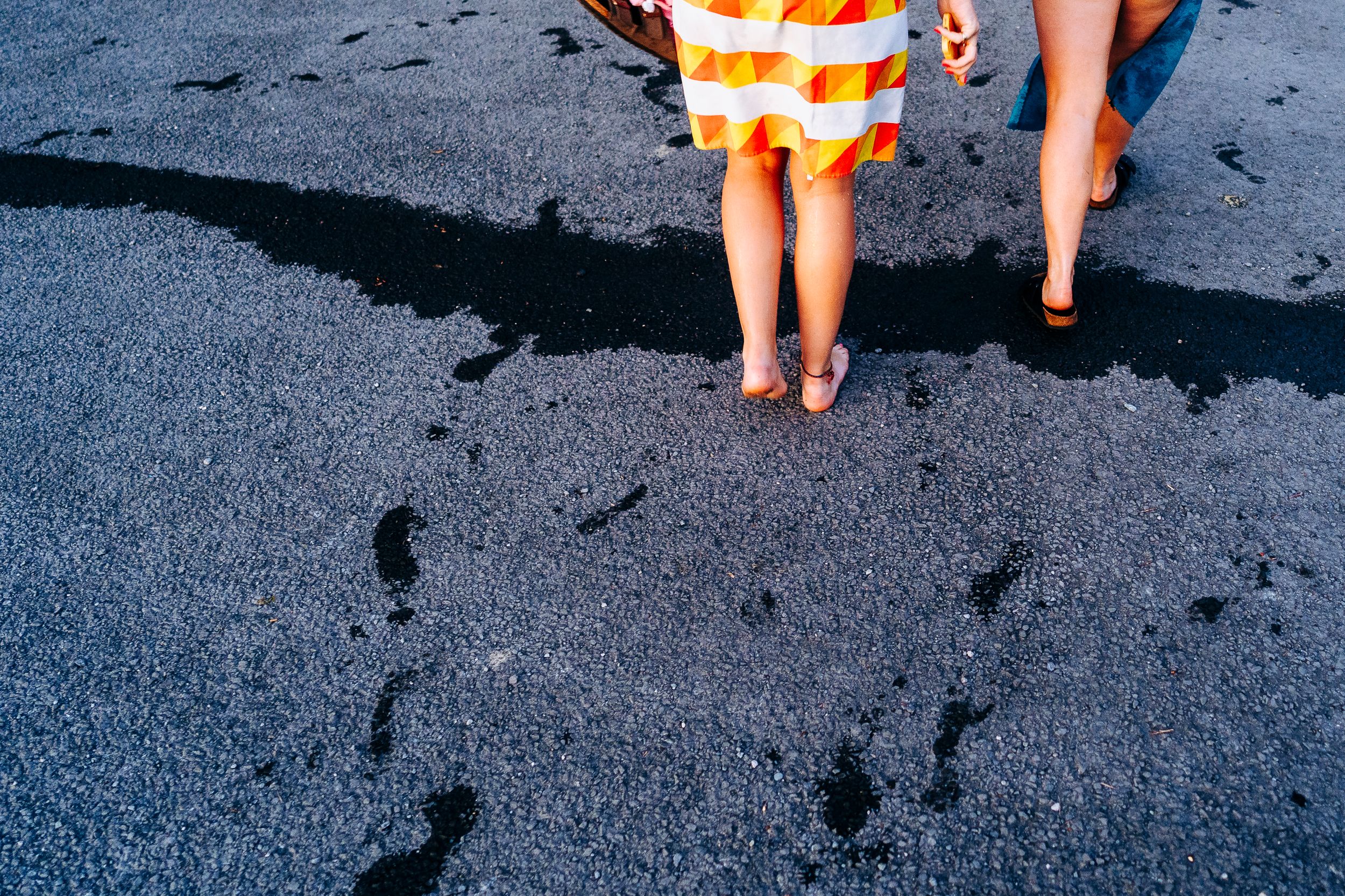 Close-up of two people walking barefoot on wet dark sand wearing a colorful striped towel.