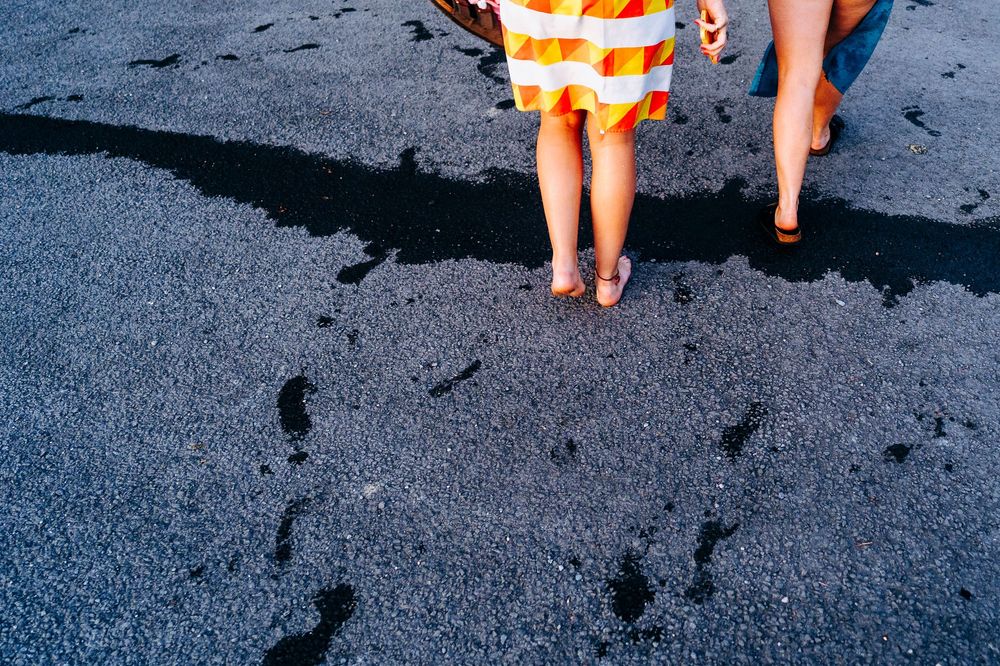 Close-up of two people walking barefoot on wet dark sand wearing a colorful striped towel.