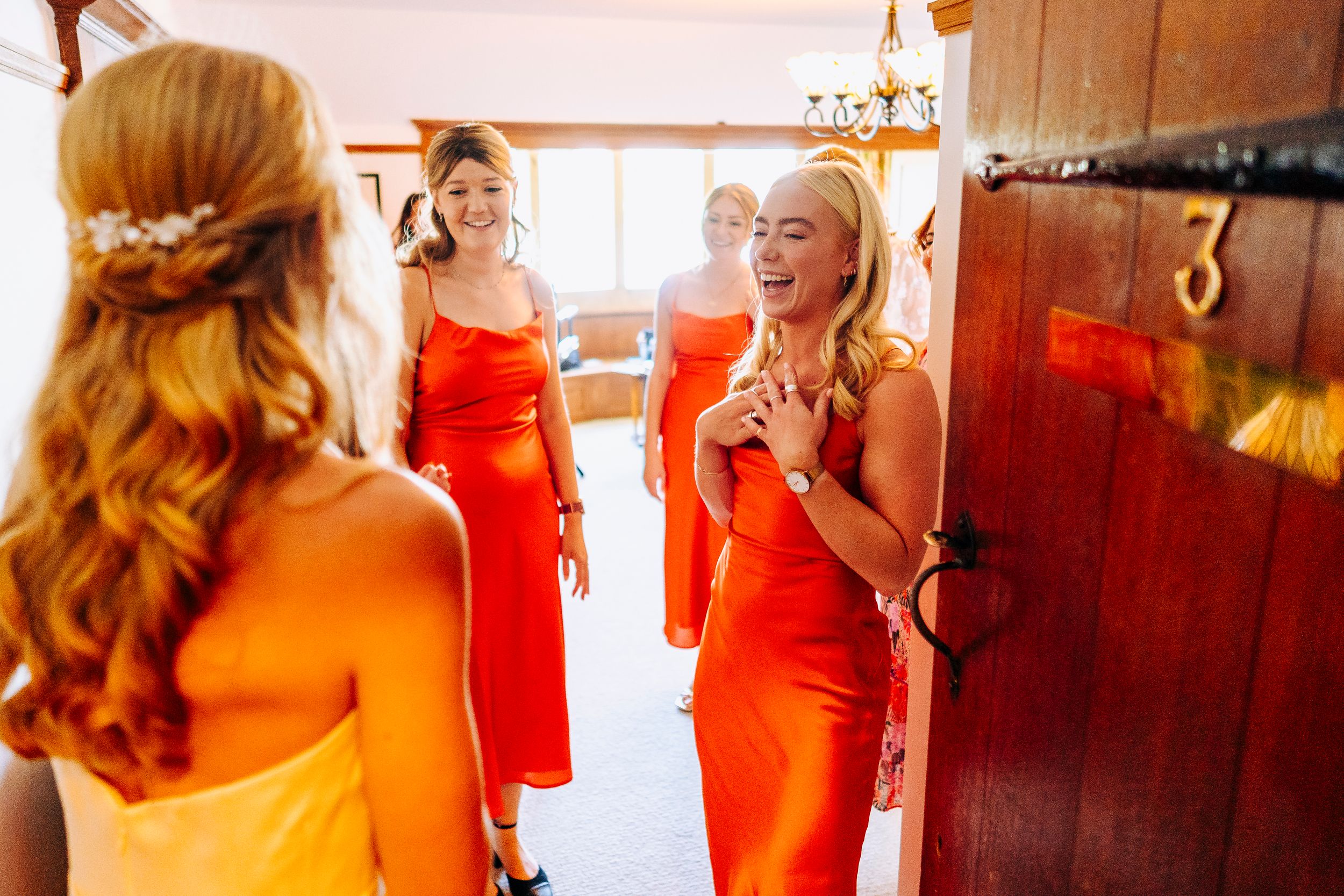 Bridesmaids in vibrant orange satin dresses laughing and celebrating together before the wedding.