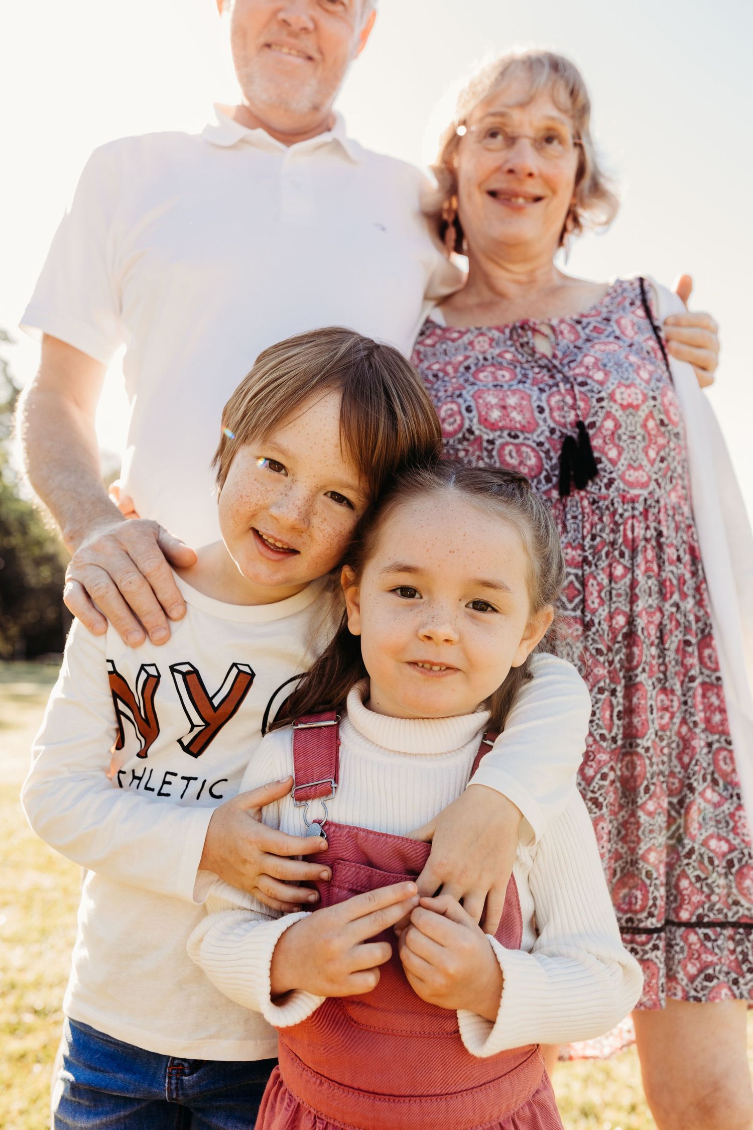 Happy family of grandparents and two young children posing outdoors in sunlight.
