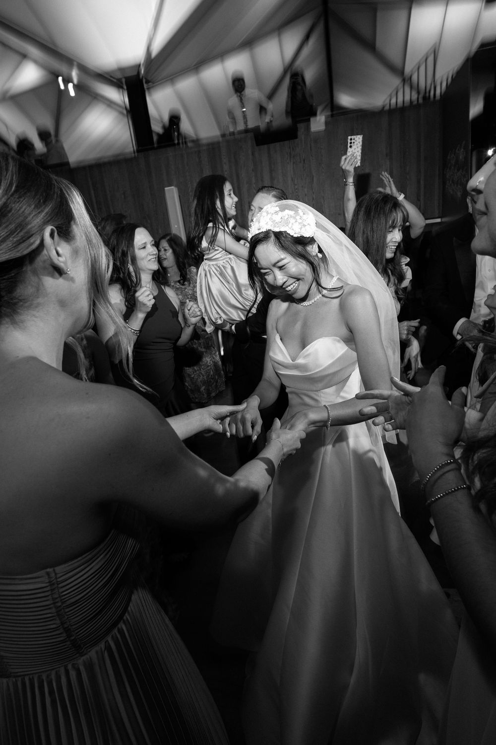 Wedding reception guests dance energetically while the bride in white dress twirls on a dark dance floor.