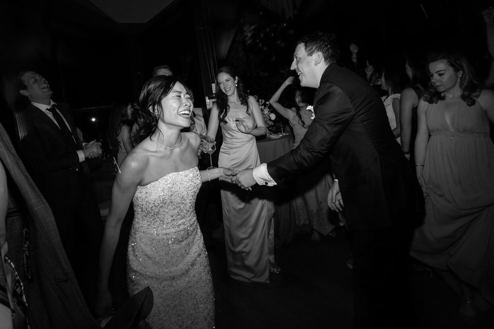 Wedding guests dancing energetically on the dance floor at a nighttime reception in black and white photography.