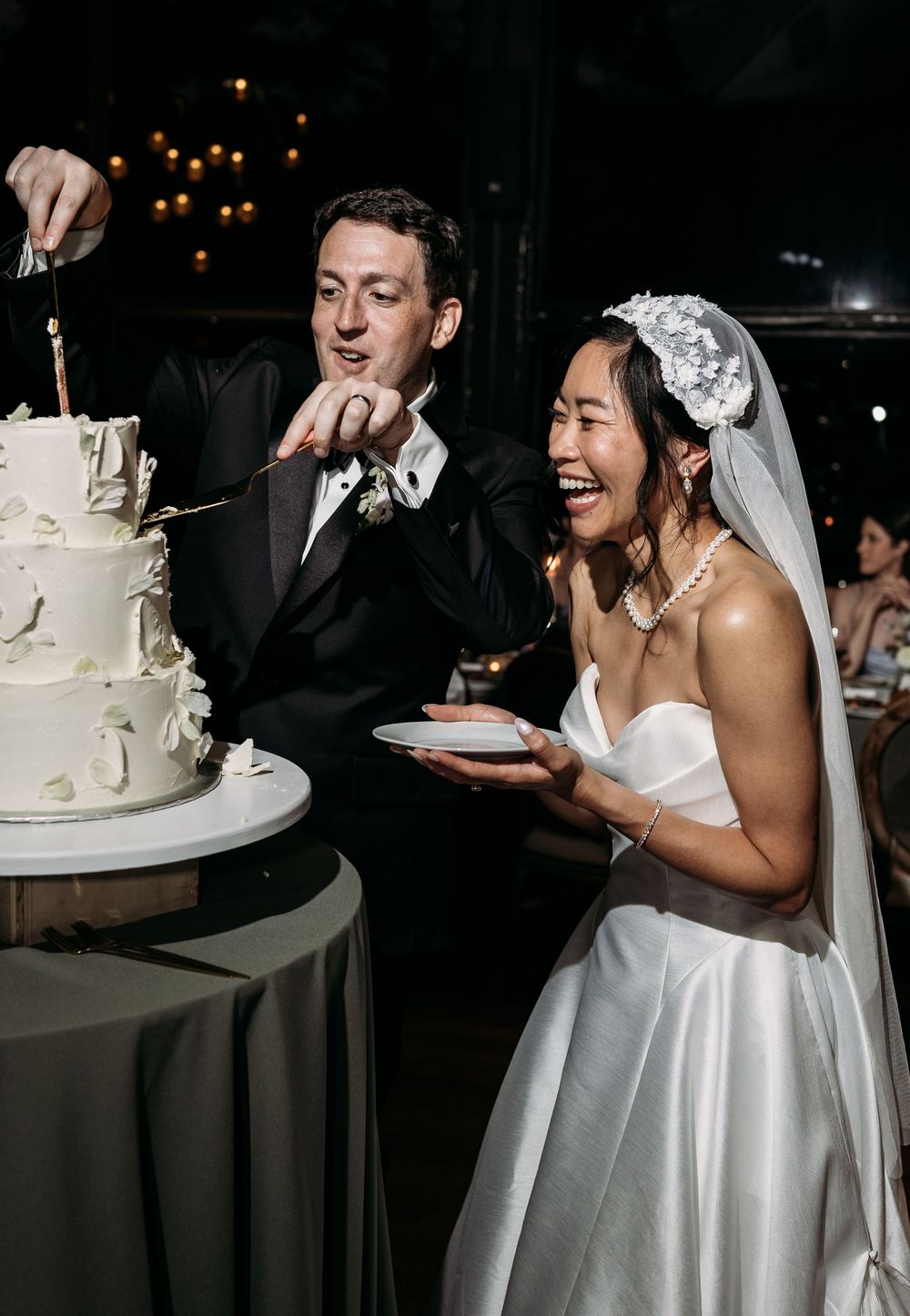 A newlywed couple shares a joyful moment while cutting their elegant white wedding cake at their reception celebration.