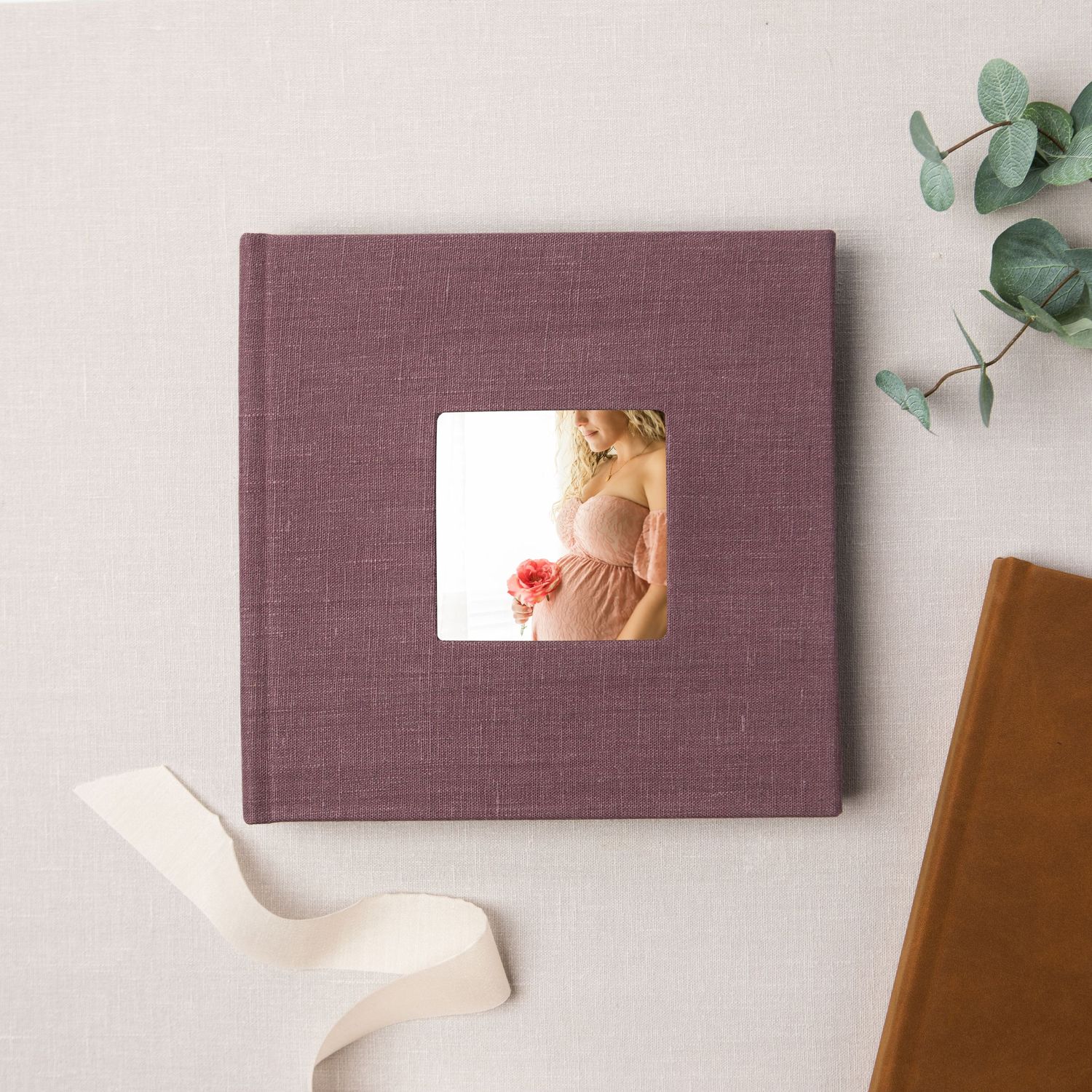 Flat lay composition showing purple hardcover photo album with eucalyptus leaves and brown leather accessories in Southlake, TX