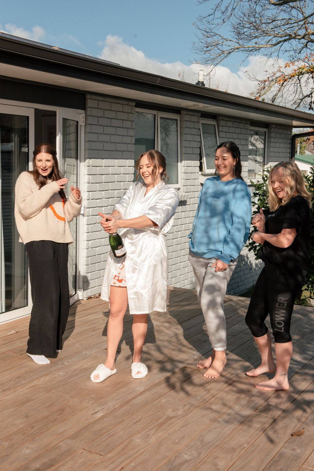 Four friends celebrate with champagne on a wooden deck during wedding preparations Cambridge New Zealand