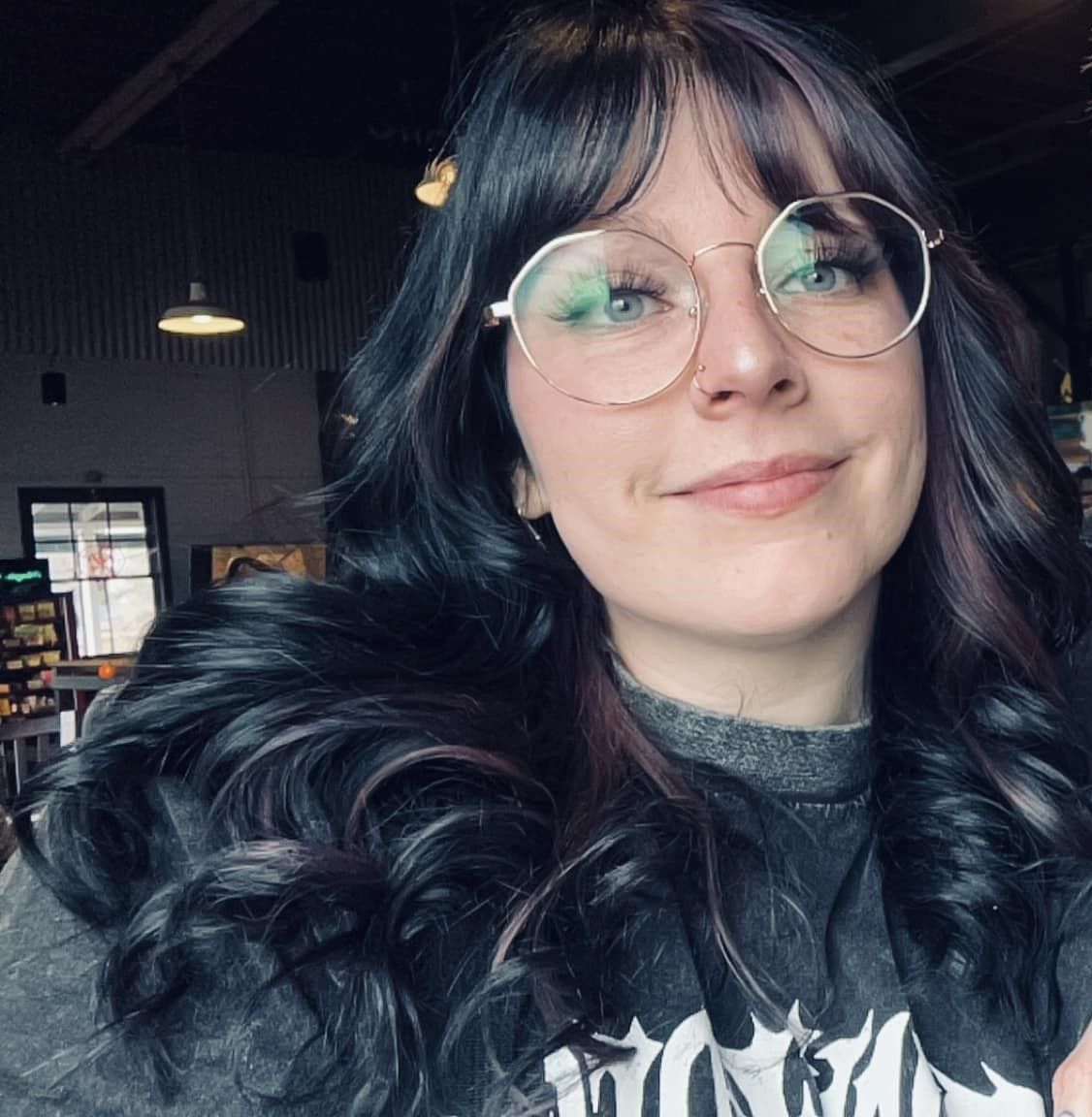 A selfie showing dark wavy hair, round glasses and a graphic t-shirt.