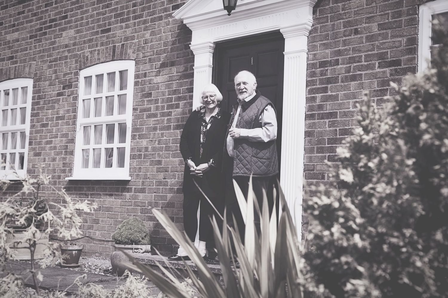 Vintage-style photo of senior couple posing by brick house with white colonial architecture. Photographer. Hull. East Yorkshire. Photography