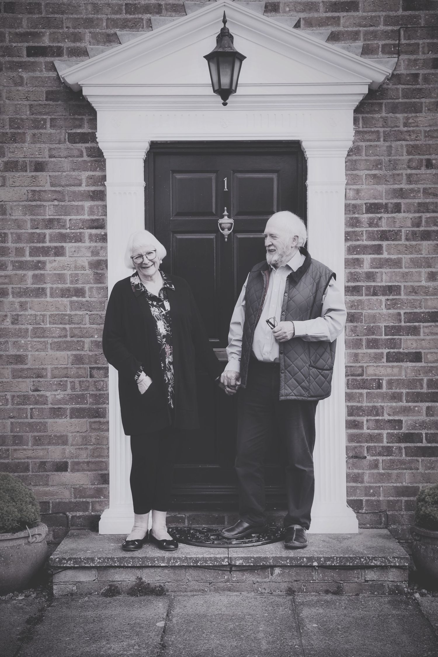 Black and white portrait of elderly couple standing in front of brick house with white doorway. Photographer. Hull. East Yorkshire. Photo
