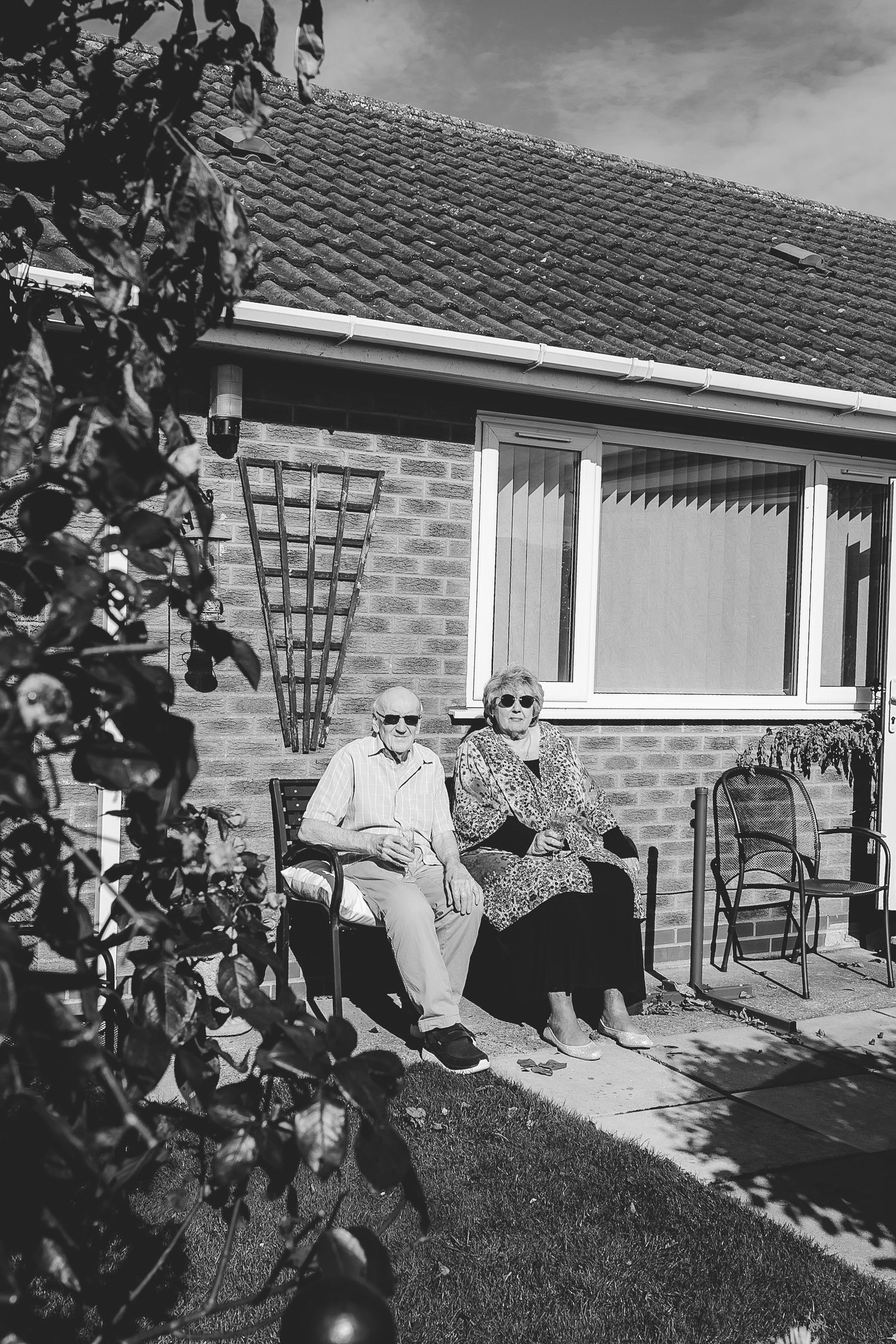 Elderly couple relaxing together on outdoor patio chairs in front of brick house. Photographer. Hull. East Yorkshire. Photography