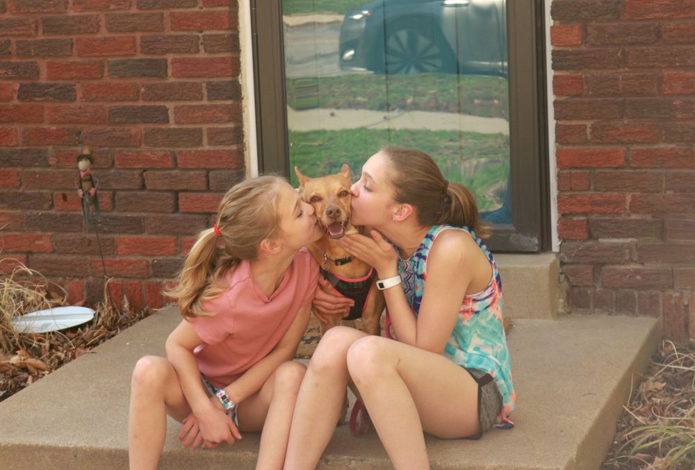 Sisters kissing their dog on the cheeks