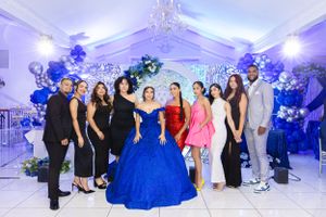 Group photo at a celebration with blue balloon arch and elegant decorations.