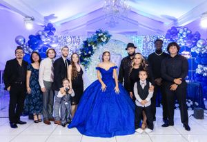 Family gathering for a formal photo with blue balloon decorations and white tent backdrop.