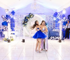 Elegant ballroom decorated in blue and white with two people dancing under a floral arch.