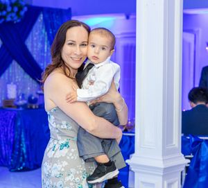 Formal event with blue decor features attendee holding small child in dressy attire.