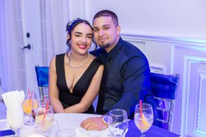 A couple smiles together at an elegant event with cocktails and blue lighting.
