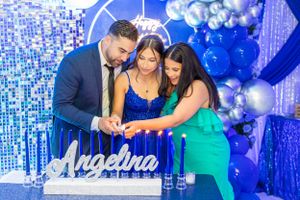 Guests gather around a decorative display with blue balloons and lighting at a celebration.