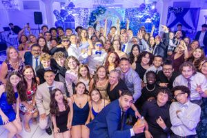 Large group of party guests pose together under blue lighting at formal event.