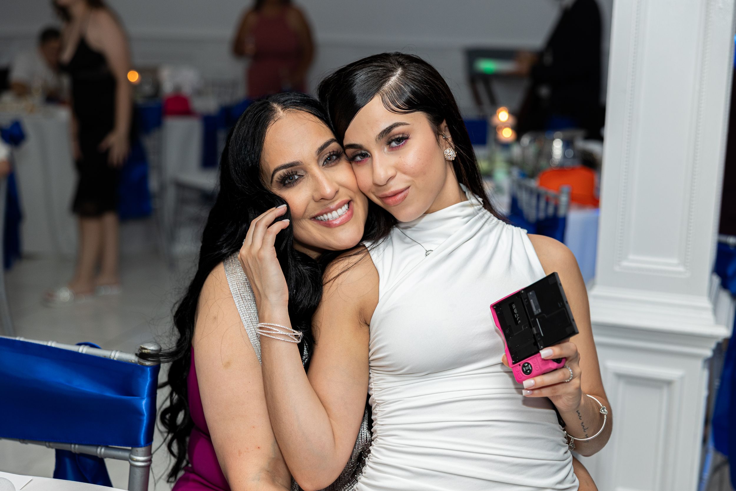 Two friends in a white outfit and black dress posing together at an event.