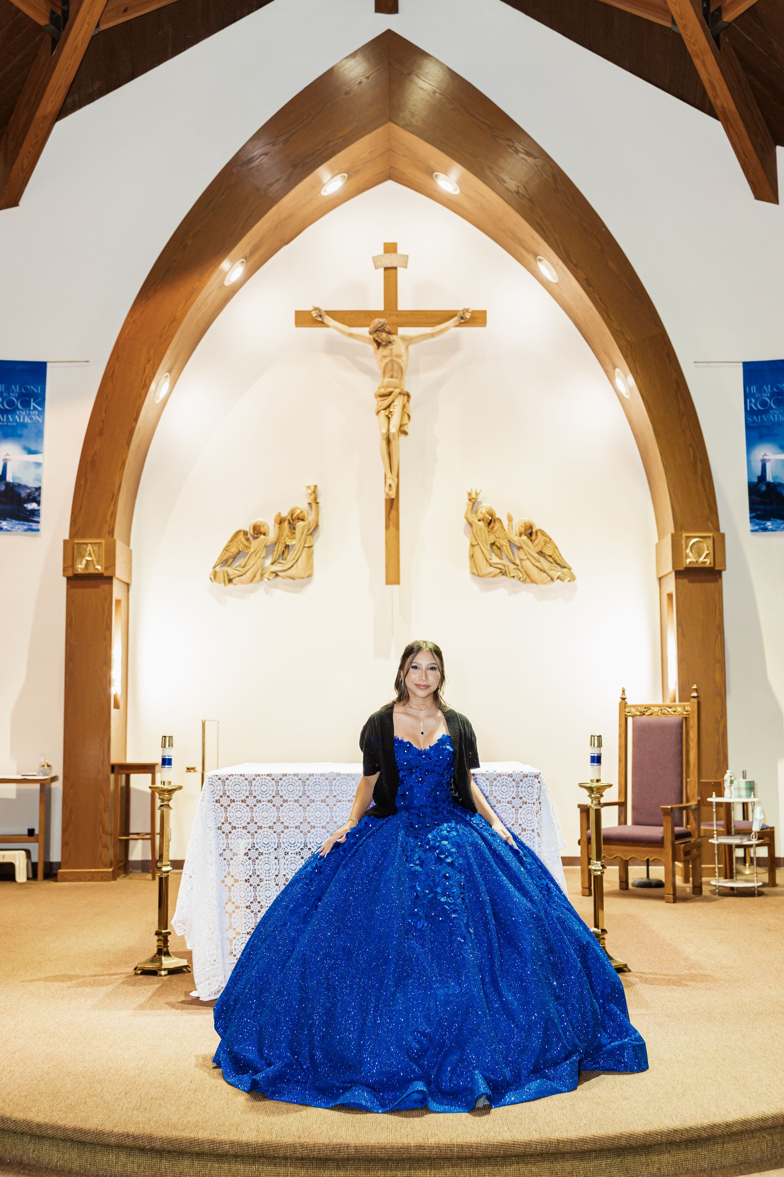 A majestic blue ballgown stands out against the white church altar with a crucifix backdrop.