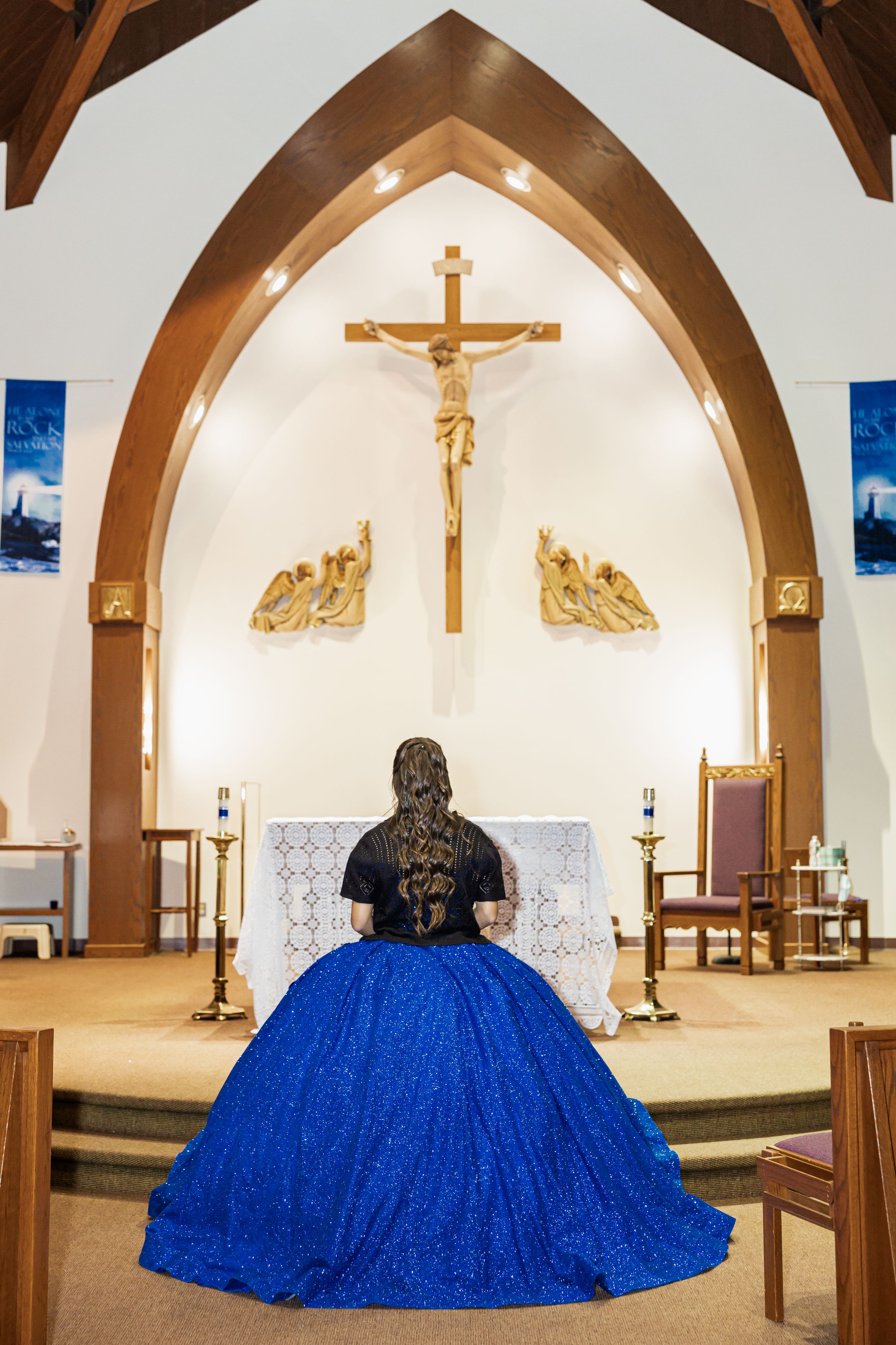 A dramatic back view of a royal blue ballgown against an illuminated church altar.