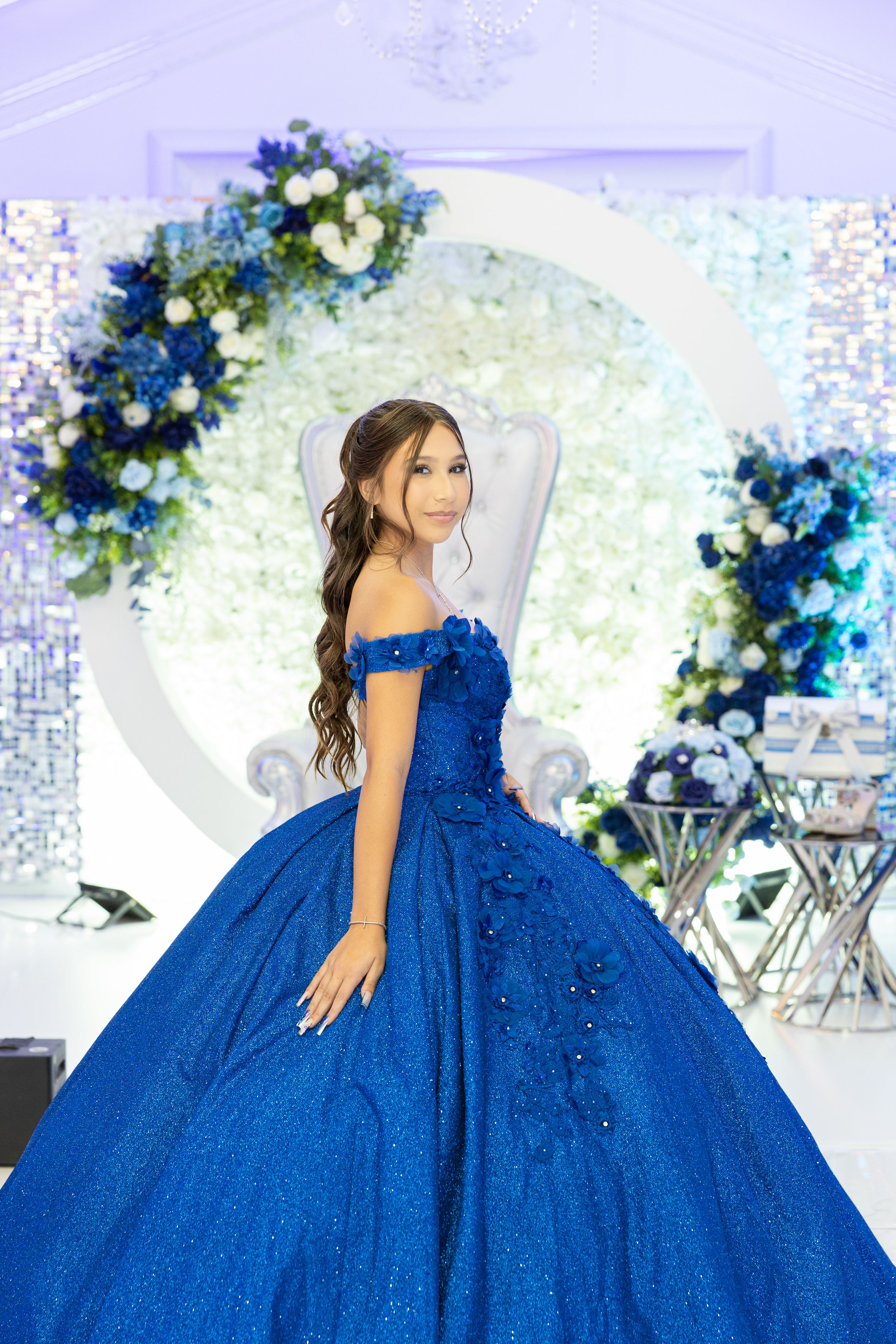 A sparkling royal blue ball gown photographed against an elegant backdrop with blue floral decorations.