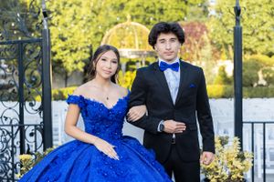 An elegant couple poses outdoors in formal attire with a blue ball gown against an autumn backdrop.
