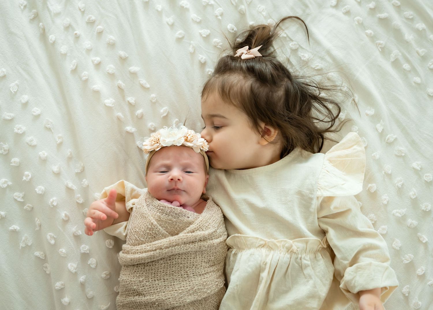 A sleeping newborn baby wrapped in a cozy beige knit blanket lies peacefully on white textured bedding.