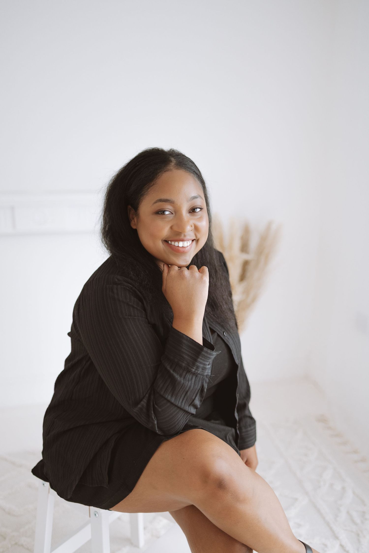 A person wearing a black sweater lounges on white bedding while smiling warmly at the camera.