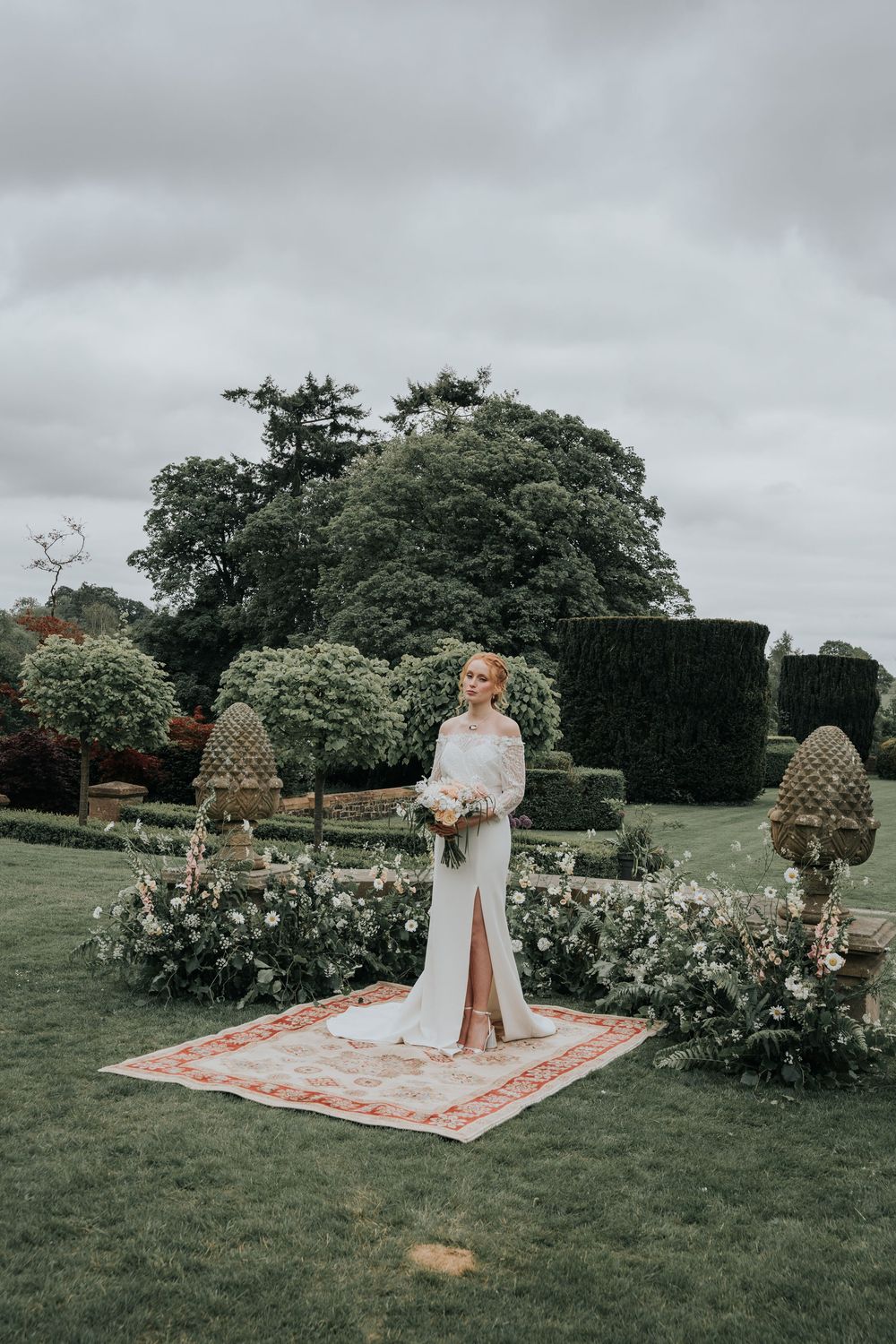 Bride sitting in the gardens at Huntsham Court surrounded by wild floral arrangements and manicured hedges