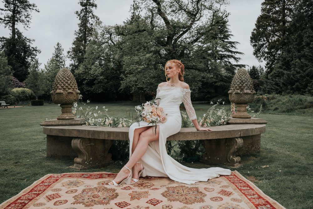 Bride sitting in the gardens at Huntsham Court surrounded by wild floral arrangements and manicured hedges