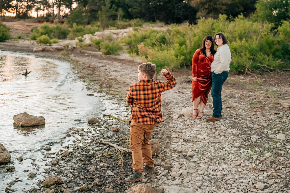 queer moms watching their son throw a rock into the grapevine lake in flower mound Texas during a lgbtq family photoshoot