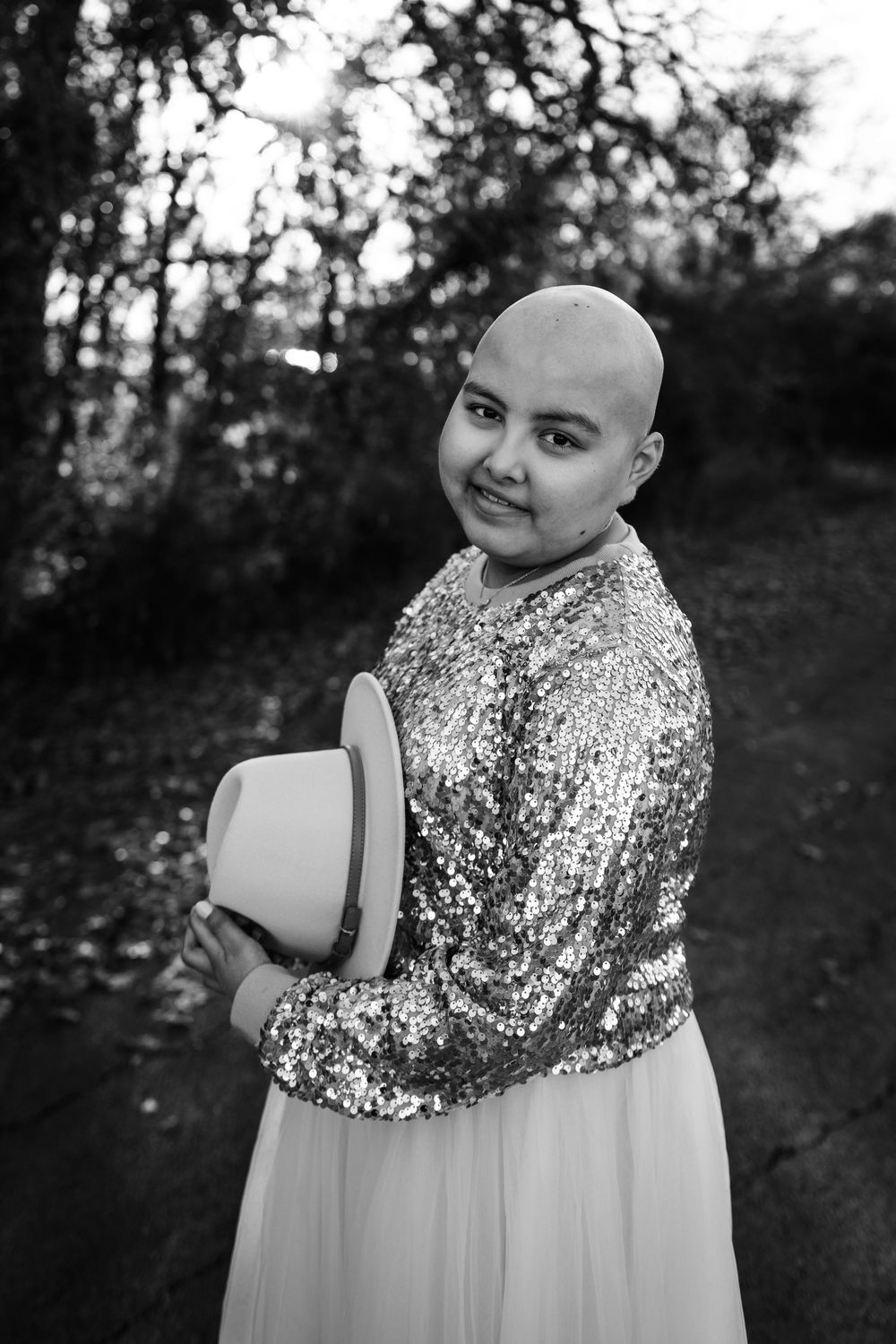 young girl with cancer smiling at camera wearing a sparkling dress holding her hat during a photoshoot in little elm Texas