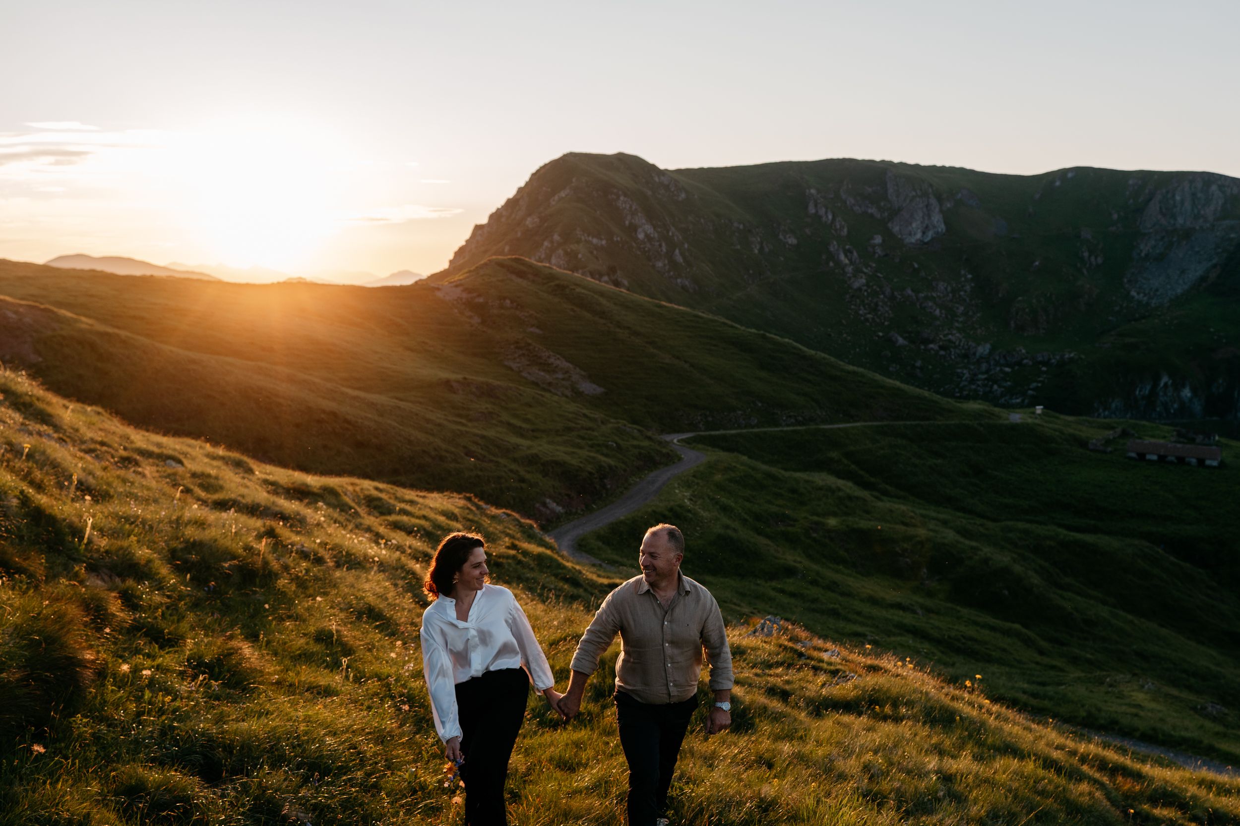 Two people hold hands while hiking along a mountain ridge at sunset.