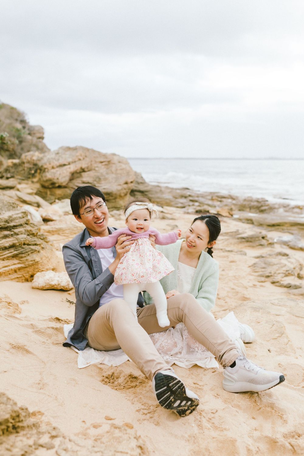 A family sits together on rocky coastal beach during overcast day, enjoying precious moments by the ocean.