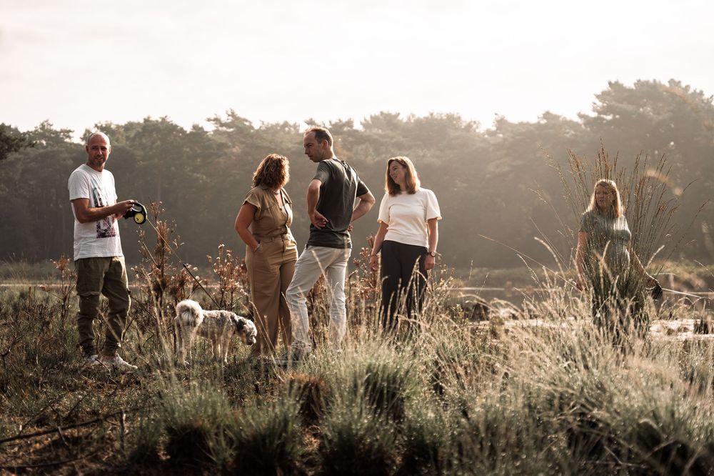 Group of people walking together through a sunlit field at golden hour with tall grass and trees in background.