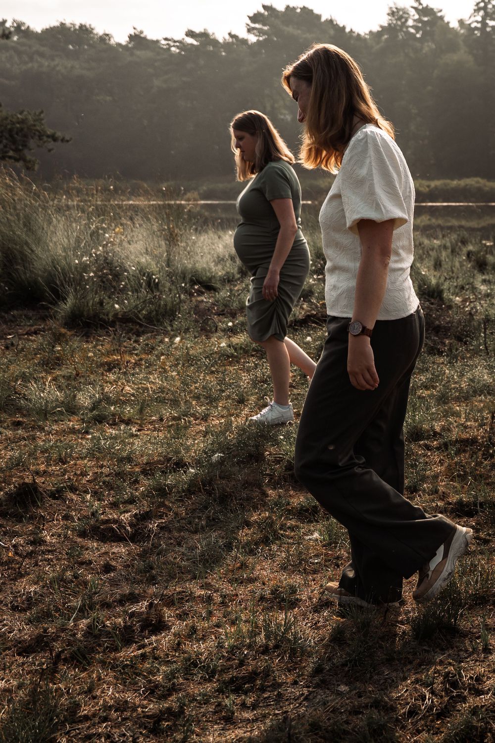 Two people walk together through a sun-drenched meadow at golden hour, creating silhouettes against the warm light.