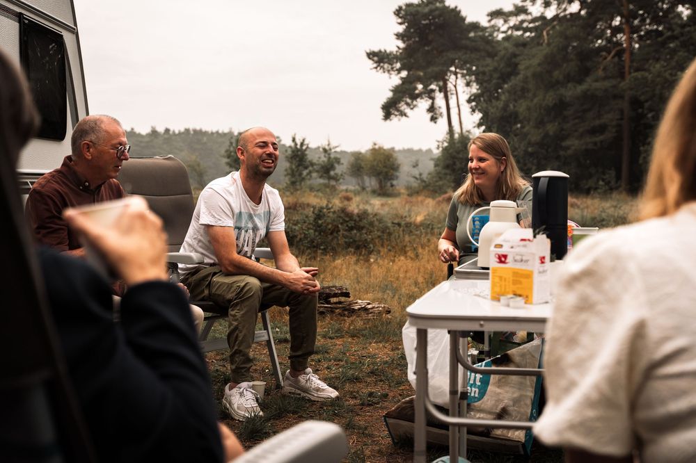 People gather around a table outdoors for a casual meal in a rustic setting at dusk.