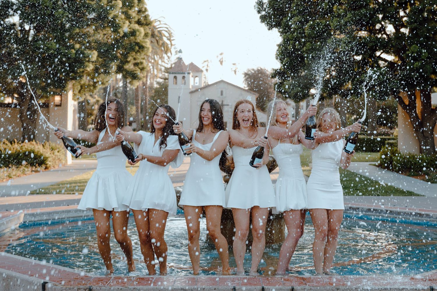 Group Santa Clara University graduate pop and spray champagne while standing in fountain. taken by Bay Area Graduation Photographer.