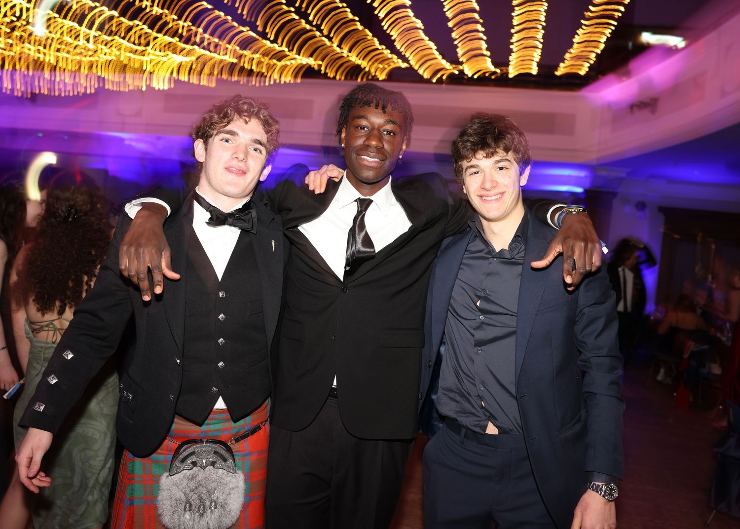 Group of people posing together at a formal event with colorful purple and pink lighting in the background.