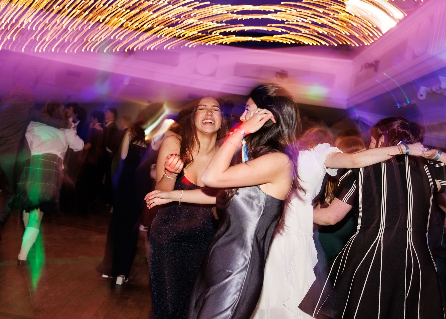 Couples dancing together at a wedding reception with colorful lighting and formal attire.
