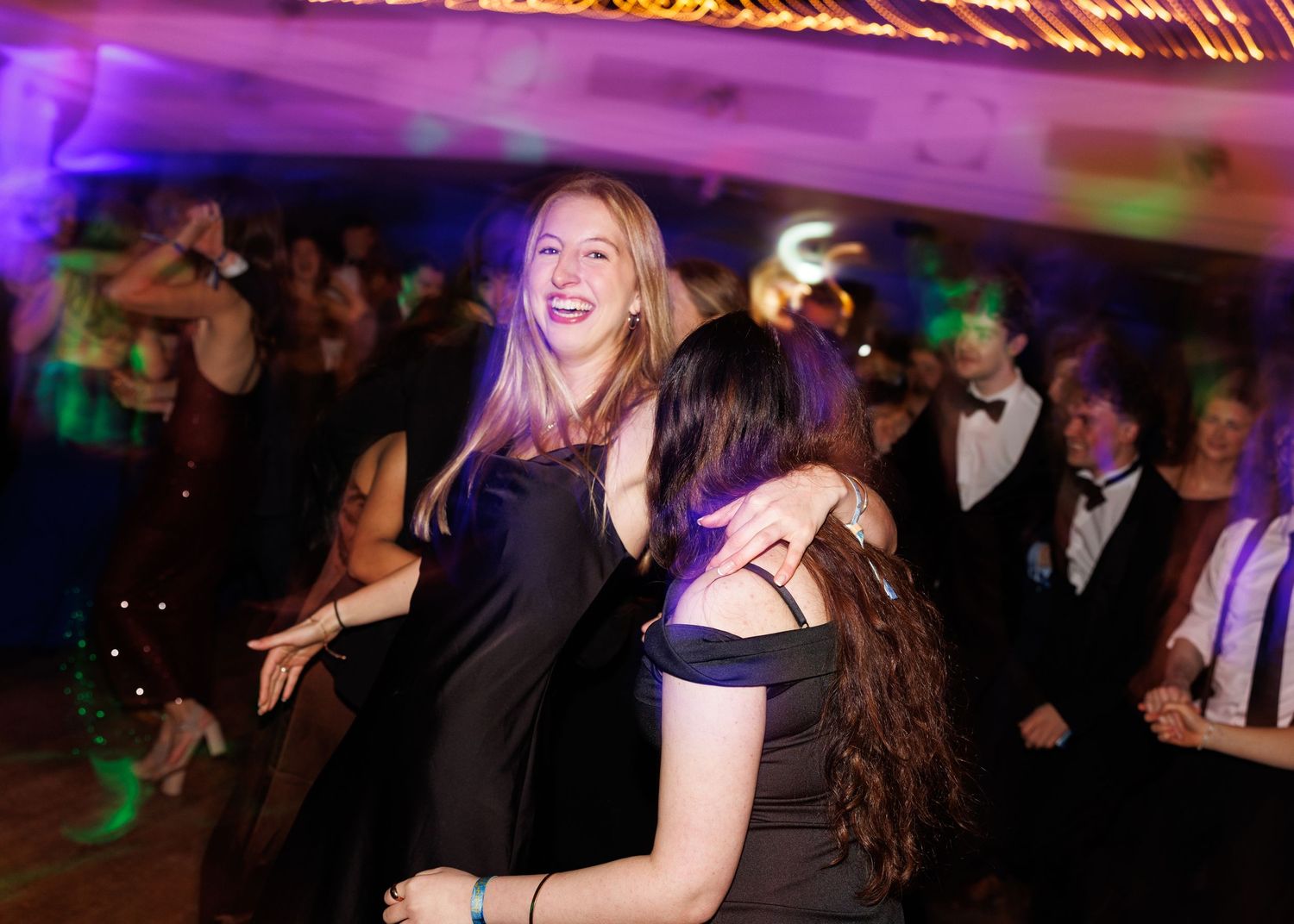 People dancing and having fun at a lively party with purple lighting and formal attire.