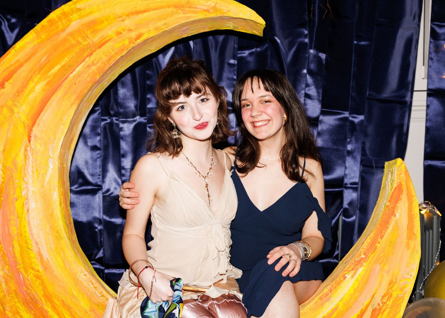 Two people pose together in front of a vibrant swirling yellow neon light display at a nighttime event.