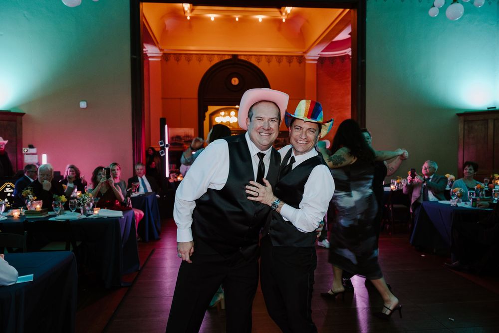 Guests dance and celebrate at a wedding reception with blue and pink lighting in an elegant ballroom.