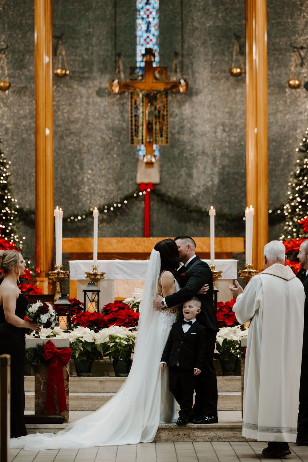 A winter wedding ceremony in a church decorated with Christmas lights and red poinsettias.