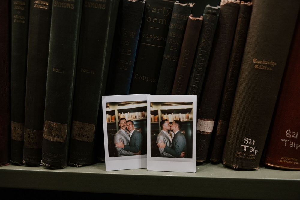 A row of vintage leather-bound books on a dark wooden shelf with small polaroid photos displayed along the top.
